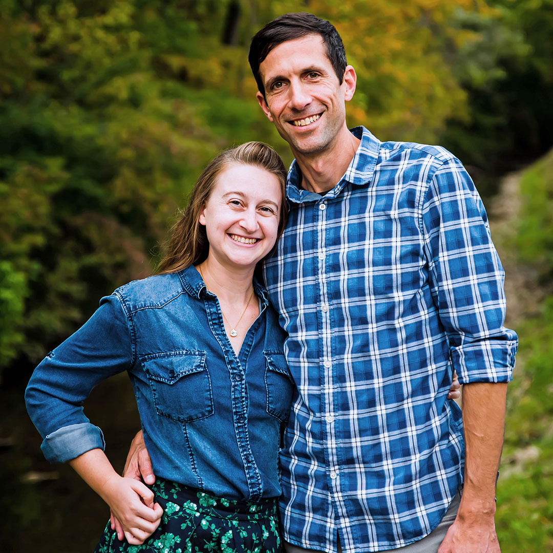 Julia Spangler and Mark Clayton smiling and standing in a green wooded setting